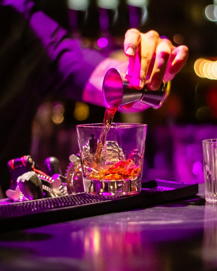 person pouring liquor in clear drinking glass